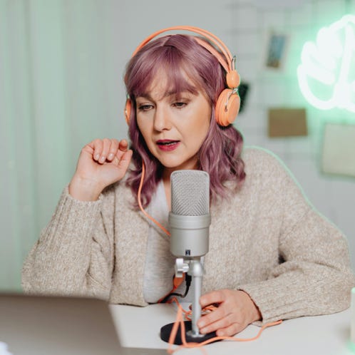 Woman podcaster in a cozy room speaking into a microphone, wearing headphones.